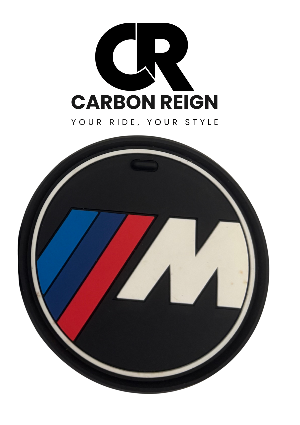 A circular black car emblem featuring the BMW M logo with blue, red, and white stripes, displayed on a white background with a Carbon Reign brand logo above it.