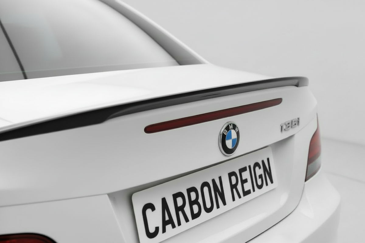 Close-up rear view of a white BMW M2 rear trunk area with a carbon-fiber-look spoiler strip above the trunk, a custom license plate reading CARBON REIGN, and the BMW roundel badge.