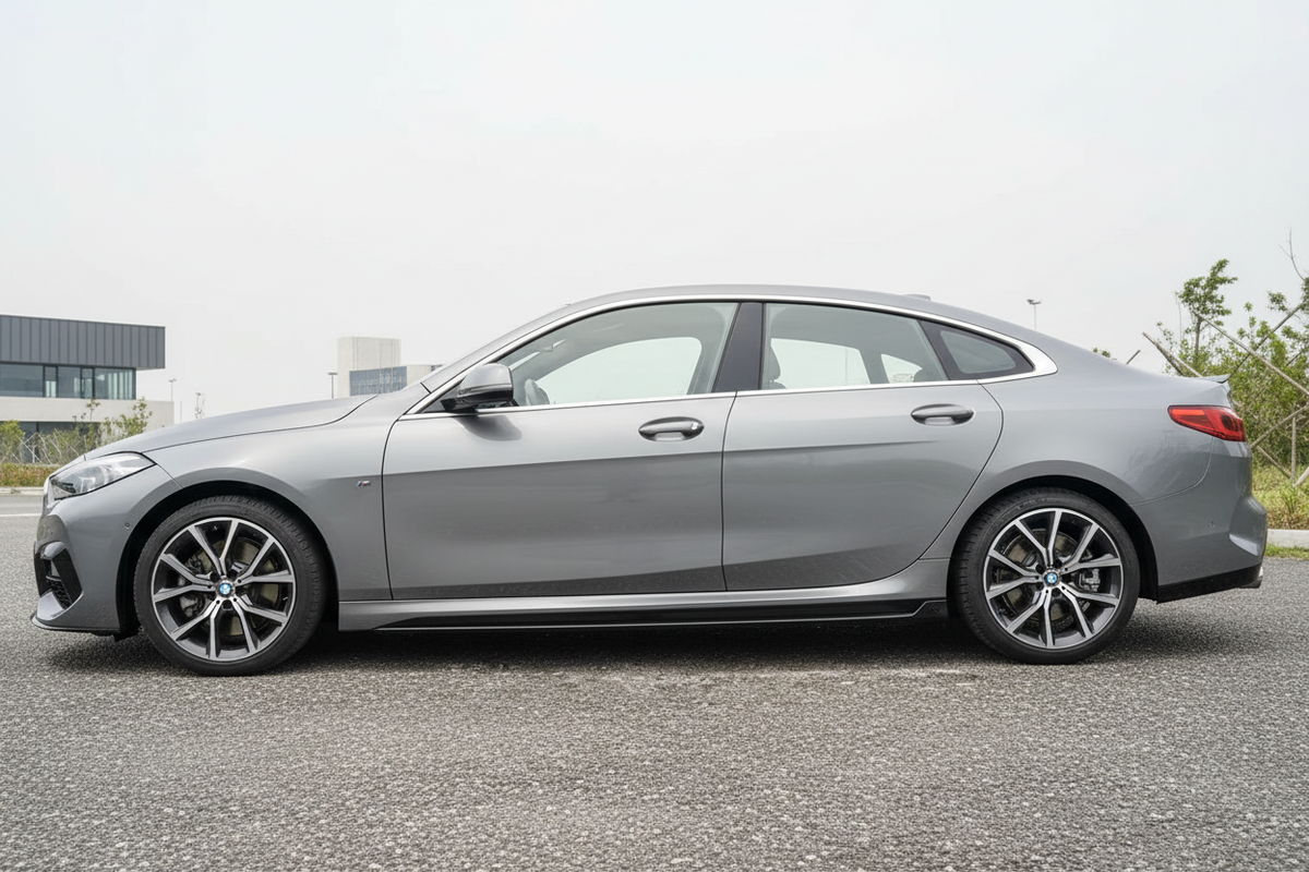 A silver BMW sedan shown from a side profile view, parked on an asphalt surface with a cloudy sky background.