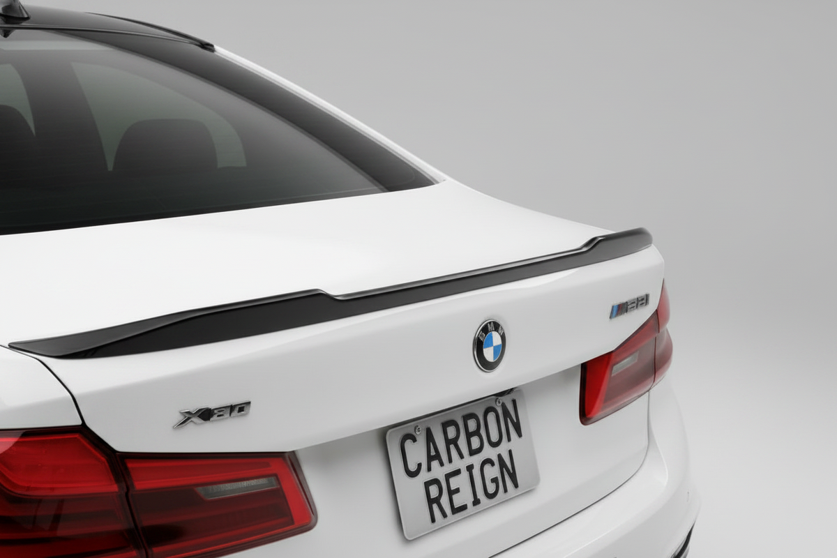 A close-up rear view of a white BMW X5 with a carbon fiber rear trunk spoiler, featuring a custom license plate that reads 'CARBON REIGN'.