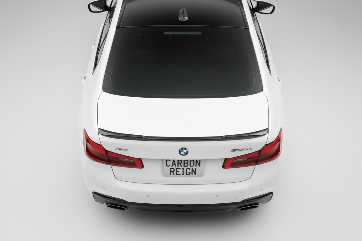 A white BMW 5 Series sedan shown from a high-angle rear view, featuring a black carbon-reinforced rear spoiler, black rear window, and a license plate that reads 'CARBON REIGN'.