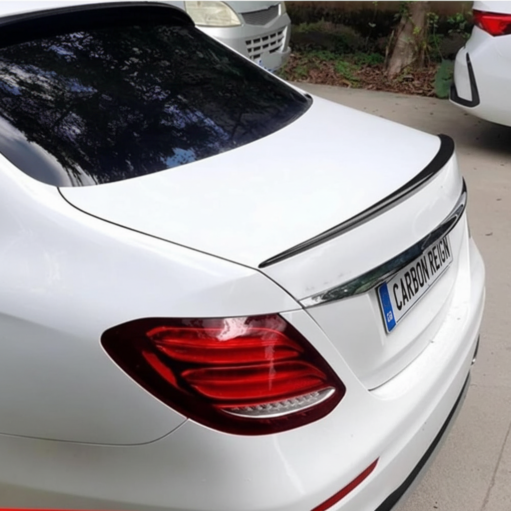 A white Mercedes-Benz sedan shown from the rear, fitted with a black trunk spoiler. The license plate reads 'CARBON REGION'.