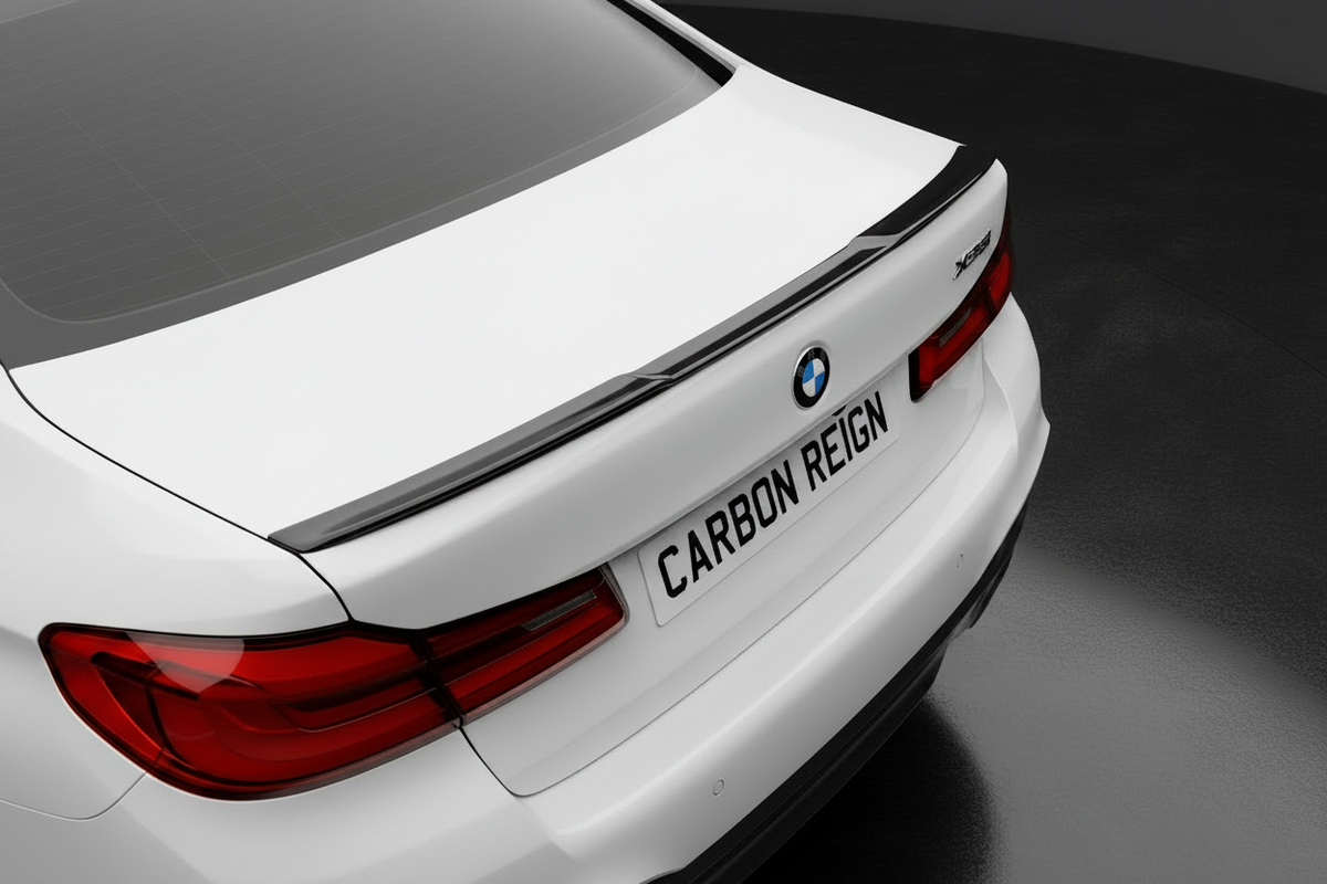 Close-up rear three-quarter view of a white BMW sedan showing the trunk, rear lights, license plate reading 'CARBON REIGN', and a dark carbon-fiber-look spoiler strip across the trunk.