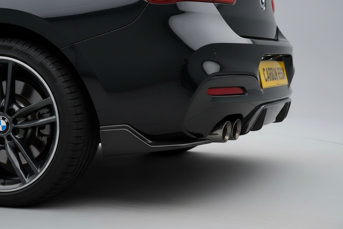 Close-up rear three-quarter view of a black BMW car showing the rear wheel, side skirt, diffuser, and dual exhaust on a light gray studio background.