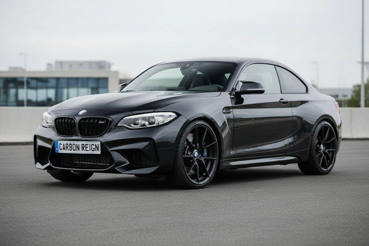A glossy black BMW M2 coupe parked outdoors on a paved surface, shown from a three-quarter front angle. The car features black wheels, a black kidney grille, and blue brake calipers, with a blurred urban background.