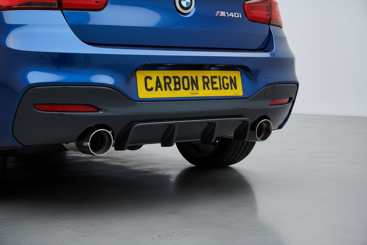 Close-up rear view of a blue BMW M140i car showing the rear diffuser, dual chrome exhaust tips, and a yellow license plate reading 'CARBON REIGN' against a clean studio background.