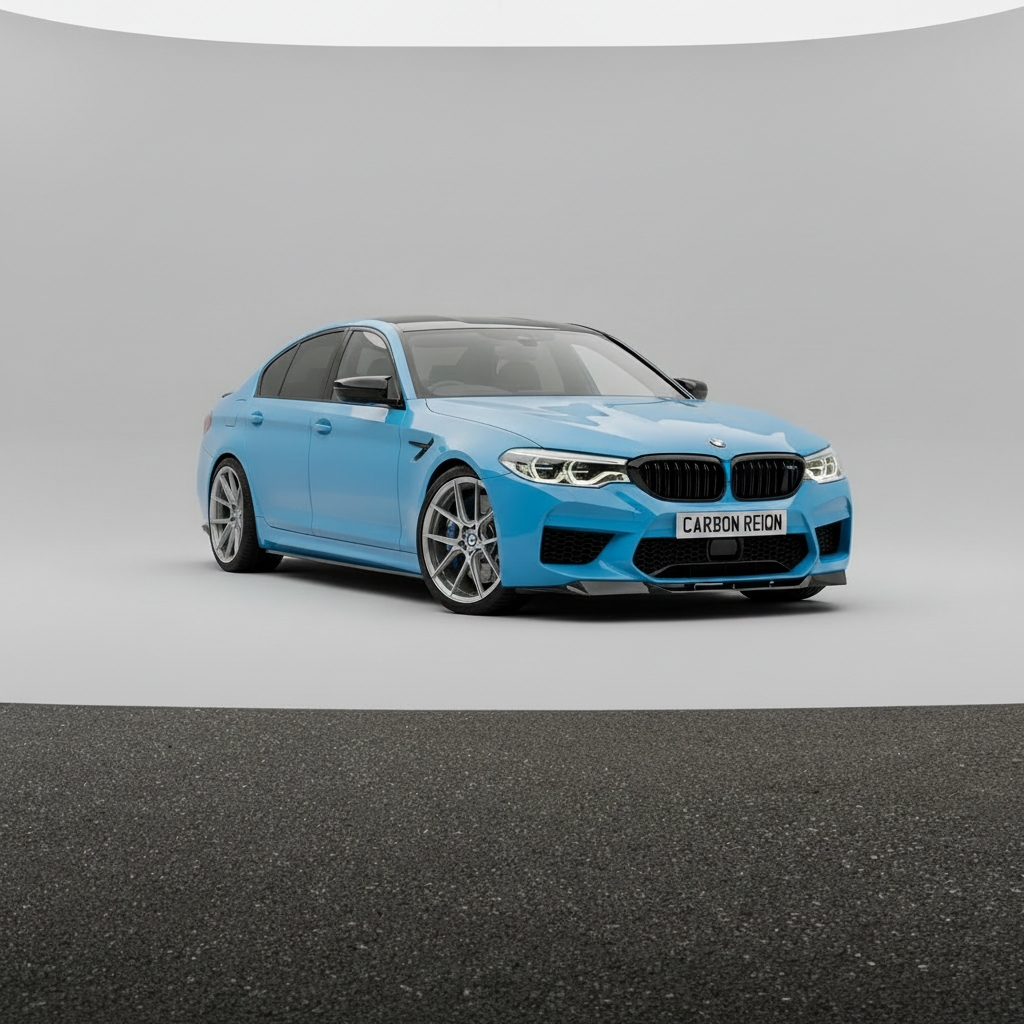 A light blue BMW M5 sedan with a carbon fiber front splitter and dark tinted glass, photographed in a studio setting with a gray background and dark asphalt-like floor.